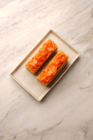 A vertical shot of a rectangular slice of multilayered orange cake with cream filling, topped with...