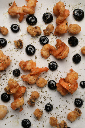 Crispy fried calamari pieces artfully arranged on a white plate with black squid ink dots, seasoning, and a lime wedge on a metallic backgroundの写真素材