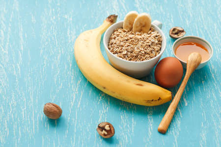 Oat flakes plate with honey, banana, egg, walnut on a turquoise wooden table. 45 degrees view of healthy oat flakes breakfast. Copy space. Selective focus.の写真素材