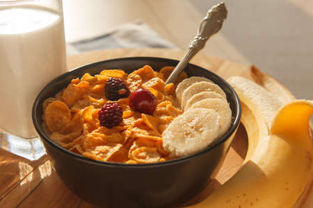 Sweet cornflakes breakfast cereal in the bowl with cherry and glass of milk on the wood table. Horizontal image. Selective focusの写真素材