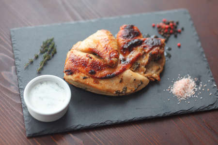 Fried chicken steak. Chicken lays on on black slate board with sprig of thyme, coarse salt and white souce. Selective focus.の写真素材