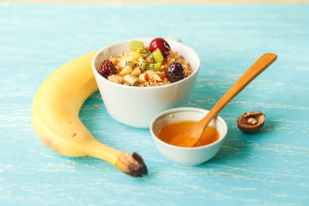 Oat flakes plate with honey, banana, egg, walnut on a turquoise wooden table. 45 degrees view of healthy oat flakes breakfast. Copy space. Selective focus.の写真素材
