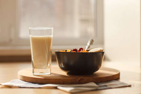 Sweet cornflakes breakfast cereal in the bowl with  cherry and glass of milk on the wood table in front of window. Horizontal image. Selective focusの写真素材