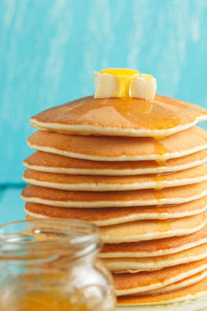 Stack of pancakes with pouring honey on plate and jar of honey on the foreground. Concept of shrovetide treats, close-up view. Selective focusの写真素材
