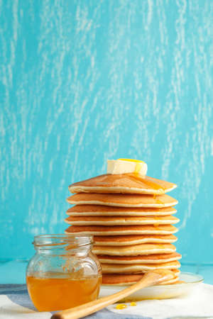 Stack of pancakes with honey and piece of butter on plate with wooden spoon and jar with honey. Copyspace. Concept of shrovetide treats. Selective focusの写真素材