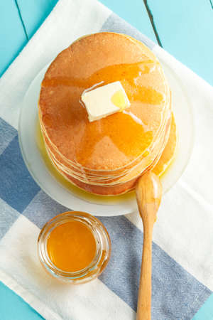 Top view of stack of pancakes with honey and butter on plate with wooden spoon and jar with honey. Concept of shrovetide treats. Selective focusの写真素材
