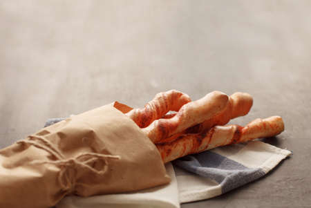 Four baguettes in wrapping paper tied with twine lie on white and blue cages napkin, on black wooden table with copyspace. Rustic kitchen or bakeryの写真素材