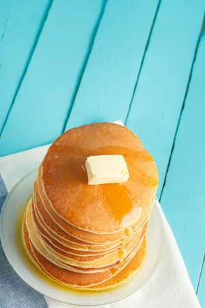 Stack of pancakes with honey and piece of butter on plate which stands on napkin on blue wooden table. Vertical photo. Copyspace. Concept of shrovetide treats. Selective focusの写真素材