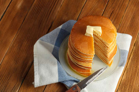 Cut stack of pancakes with honey and butter on top stands on plate with knife on wooden table. Copyspace. Top view. Concept of shrovetide treats. Selective focusの写真素材