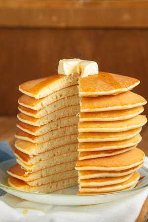 Cut stack of pancakes with honey and piece of butter on plate which stands on napkin on wooden table. Copyspace. Close up Concept of shrovetide treats. Selective focusの写真素材