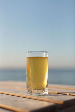 Glass of cold drink on sunbed or wooden table on sea and sky background. Vertical image with copyspaceの写真素材