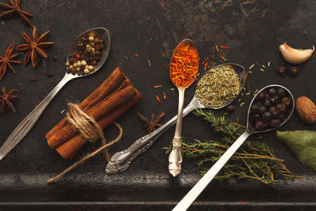 Plenty of herbs and spices in metal spoons and around on dark old table or background with copysapce for menu. Vertical image. Top view. Dark moody photoの写真素材