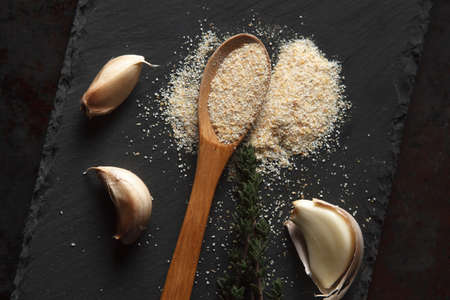 Close up composition of garlic powder sprinkled into wooden spoon, two sprigs of thyme and three cloves on black slate board. Selective focusの写真素材