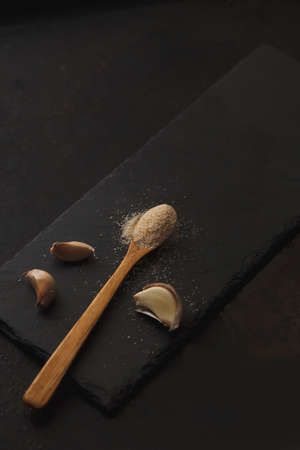 Photo with garlic powder sprinkled into wooden spoon and three cloves on dark slate board. Copyspace. Selective focusの写真素材