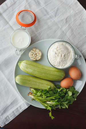 Ceramic plate with squash, garlic, parsley, two eggs, flour and sour cream near on wooden table. Ingredients for salad or garnishの写真素材