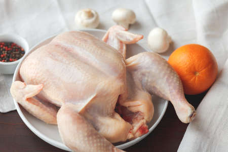 Raw chicken on a white plate, spices and mushrooms with orange near on a dark wooden table, selective focus. Healthy food or cooking conceptの写真素材