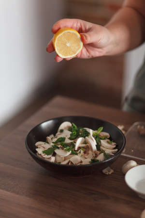 Woman squeezing lemon to salad with mushrooms and herbの写真素材