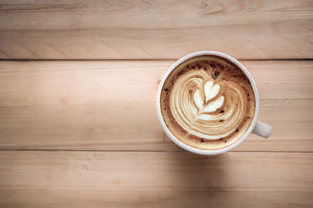 A cup of coffee latte art with heart pattern in a white cup on wooden background. Top view latte art coffeeの写真素材