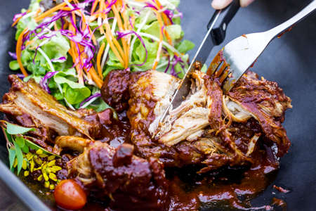 Steak knife and fork slicing grilled rib eye beef steak with vegetable salad in black bowlの写真素材
