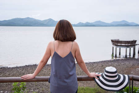 Young woman standing on terrace and looking the mountains above sea, rear viewの写真素材