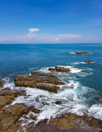 Waves crashing on the black rocks beneath a blue sky at Koh Kham Tok Island Ranong Province, Thailand. Andaman seaの写真素材