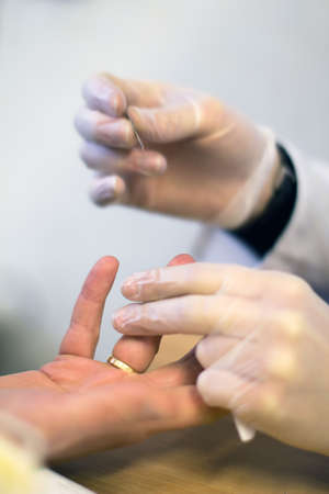 A doctor is doing his job. He uses needle to make a little dimple in patient's finger, so he could...