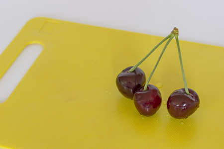three cherries just washed on the yellow trayの写真素材