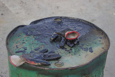 Safety glove covered in bitumen laying on the top barrel of bitumenの写真素材