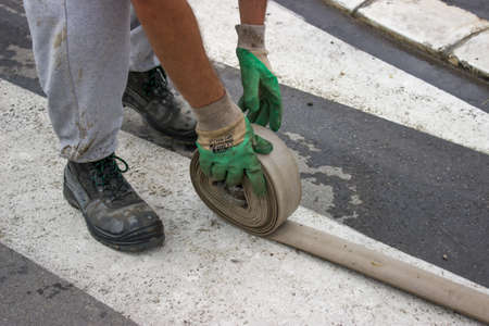 Man rolling up a fire hose after filled 500 Litre Water Tanksの写真素材