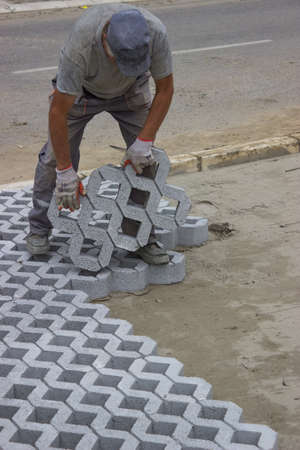 Worker paving new parking places, concrete grid pavers can be filled with soil for grass growth or aggregate for drainage applications.の写真素材