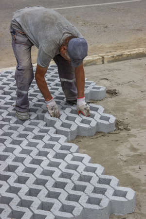 Worker paving new parking places, concrete grid pavers can be filled with soil for grass growth or aggregate for drainage applications.の写真素材