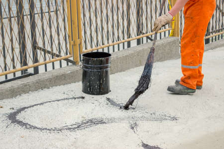 Asphalt worker apply tack coat with a broom to a concrete before paving. Asphalt tack coat is used to ensure a good bond.の写真素材
