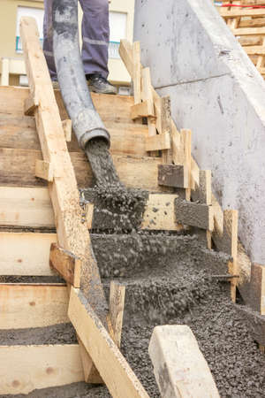 manual workers pouring concrete steps with tube from truck mounted concrete pumpの写真素材