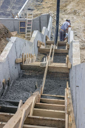 manual workers pouring concrete steps with tube from truck mounted concrete pumpの写真素材