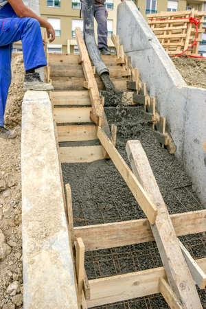 manual workers pouring concrete steps with tube from truck mounted concrete pumpの写真素材
