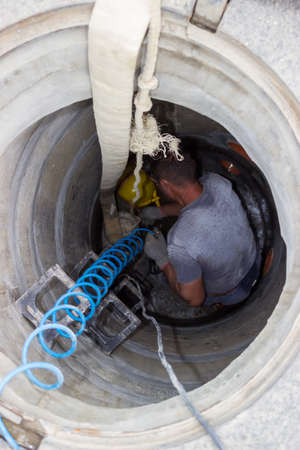 A man in manhole on street, using a air compressor hose for repairs inside a manholeの写真素材