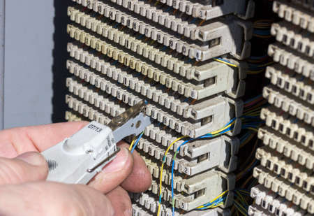 Close of hands punching down circuit panel used for phones. Using a punch down tool punch the wires down into the blades built into the communication circuit for analog phones.の写真素材