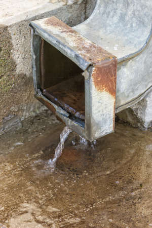 Rain water from rusty downspout. Water flow from metal drain pipe. Selective focus.の写真素材