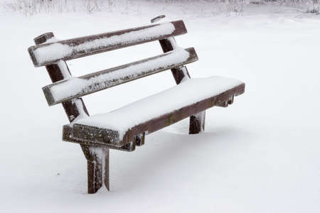 snow covered wooden sitting bench in park at winterの写真素材