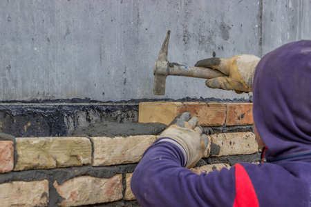 Close up of worker hands using mason hammer to tap brick into position. Selective focus.の写真素材