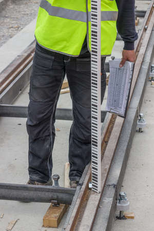 Measuring height by optical levelling. Worker installing tram track and measuring level with...