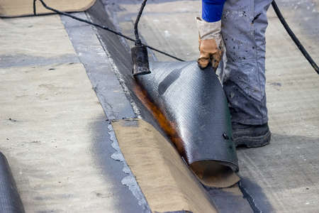 Insulation worker with propane blowtorch at floor slab insulation work. Worker heating and melting bitumen felt.の写真素材