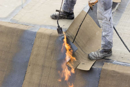 Insulation worker with propane blowtorch at floor slab insulation work. Worker heating and melting roll of bitumen roll.の写真素材
