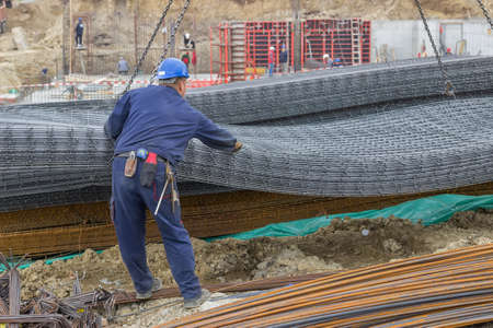 Iron worker unloading reinforcing steel from crane for construction. At construction site.