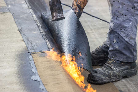 Insulation worker with propane blowtorch at floor slab insulation work. Worker heating and melting...