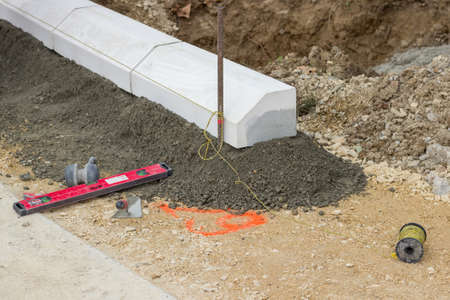 Tools for installing concrete curb stone and string with metal stakes to level at sidewalk construction site. Selective focus.の写真素材