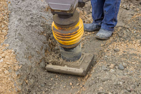 worker compacting the sand bedding with mechanical rammer along the bottom of the cable trenchの写真素材