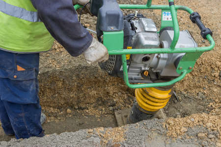 Worker with trench rammer, compacting the sand bedding spread along the bottom of the cable trenchの写真素材