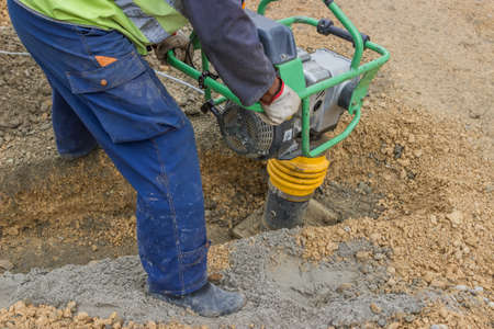 worker with trench rammer, compacting the sand bedding spread alon the bottom of the cable trenchの写真素材