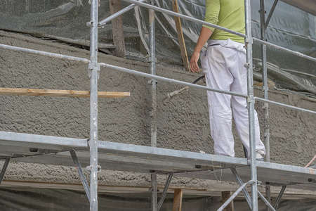 Applying mortar with the spray gun, working outside on scaffolding. Apply the mortar onto the wall in high efficiency, and save a lot of labor cost. Selective focus.の写真素材